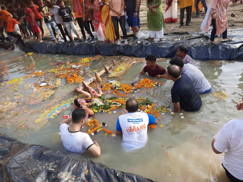 An idol of the Goddess Durga is just visible as it is immersed into the water of an artificial pond, as flowers float on the surface around it